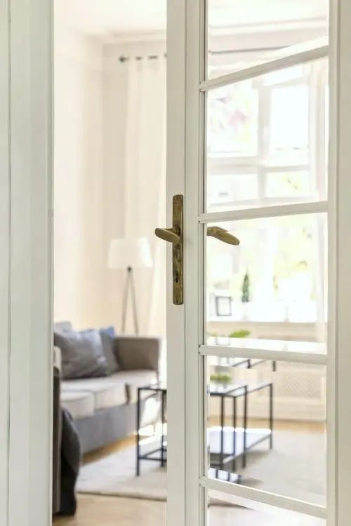 halboffene Wohnzimmertür in einer Altbauwohnung mit grauem Sofa, Teppich und Stehleuchte