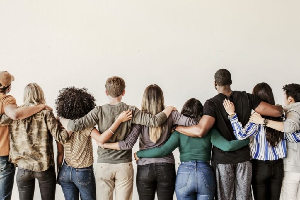 Gruppe von Menschen unterschiedlicher Herkunft steht Seite an Seite in einer Reihe und legt die Arme umeinander