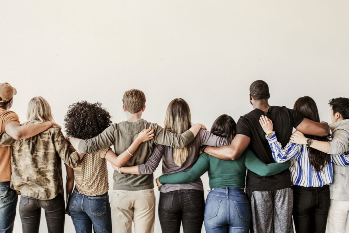 Gruppe von Menschen unterschiedlicher Herkunft steht Seite an Seite in einer Reihe und legt die Arme umeinander