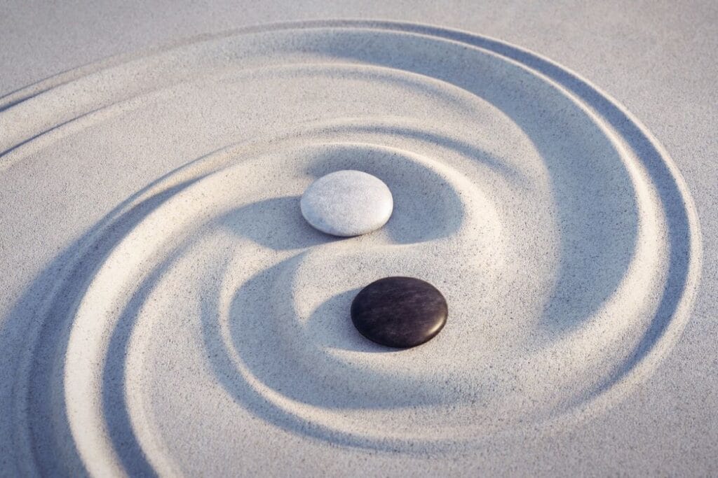 Weißer und schwarzer Stein in einer spiralförmigen Spur im Sand als Symbol für Yin und Yang